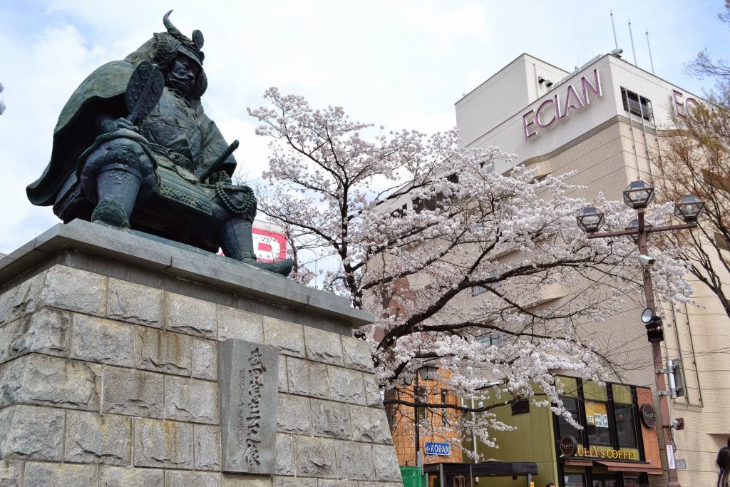 桜咲く季節の武田信玄公銅像（駅ビルは旧「エクラン」）